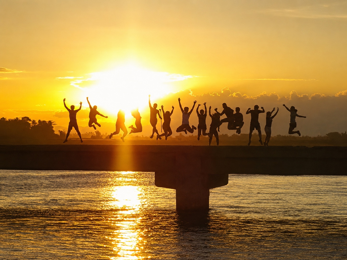 Silhouettes of friends jumping on a bridge against a golden Philippine sunset